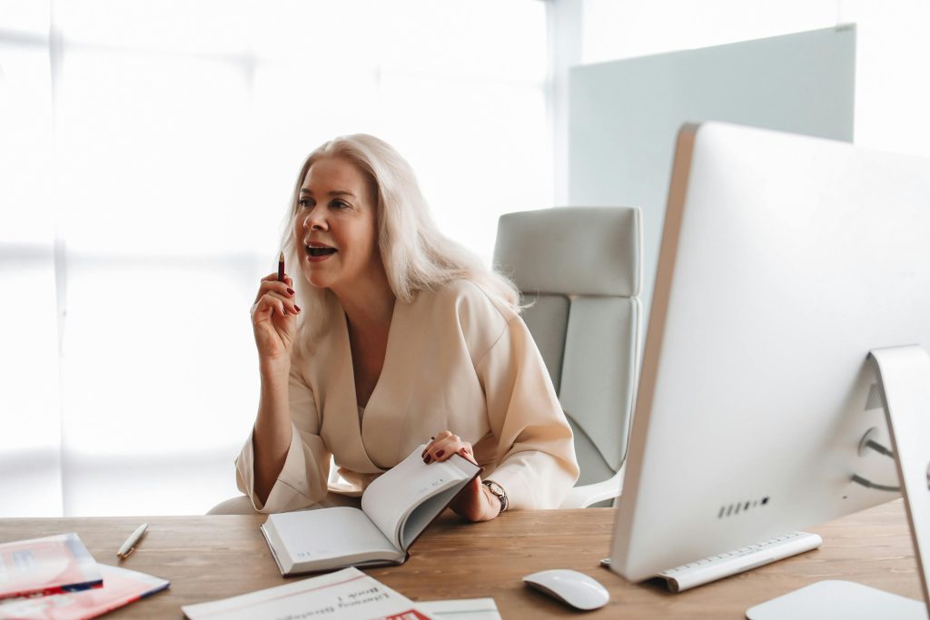 A professional woman engaged in work at a modern office desk with a computer and open books.